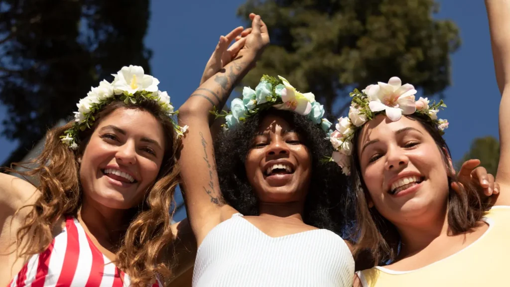 Amigas sorrindo com coroas de flores em uma festa primavera ao ar livre