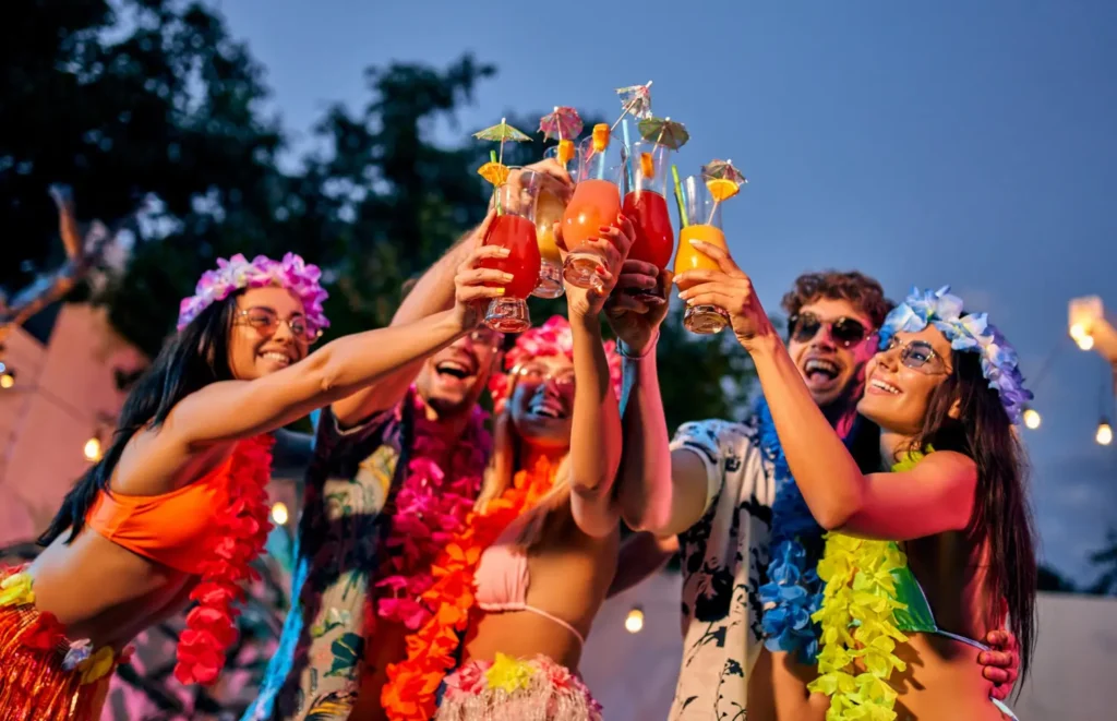 Grupo brindando com drinks coloridos usando colares de flores em uma festa havaiana ao ar livre à noite